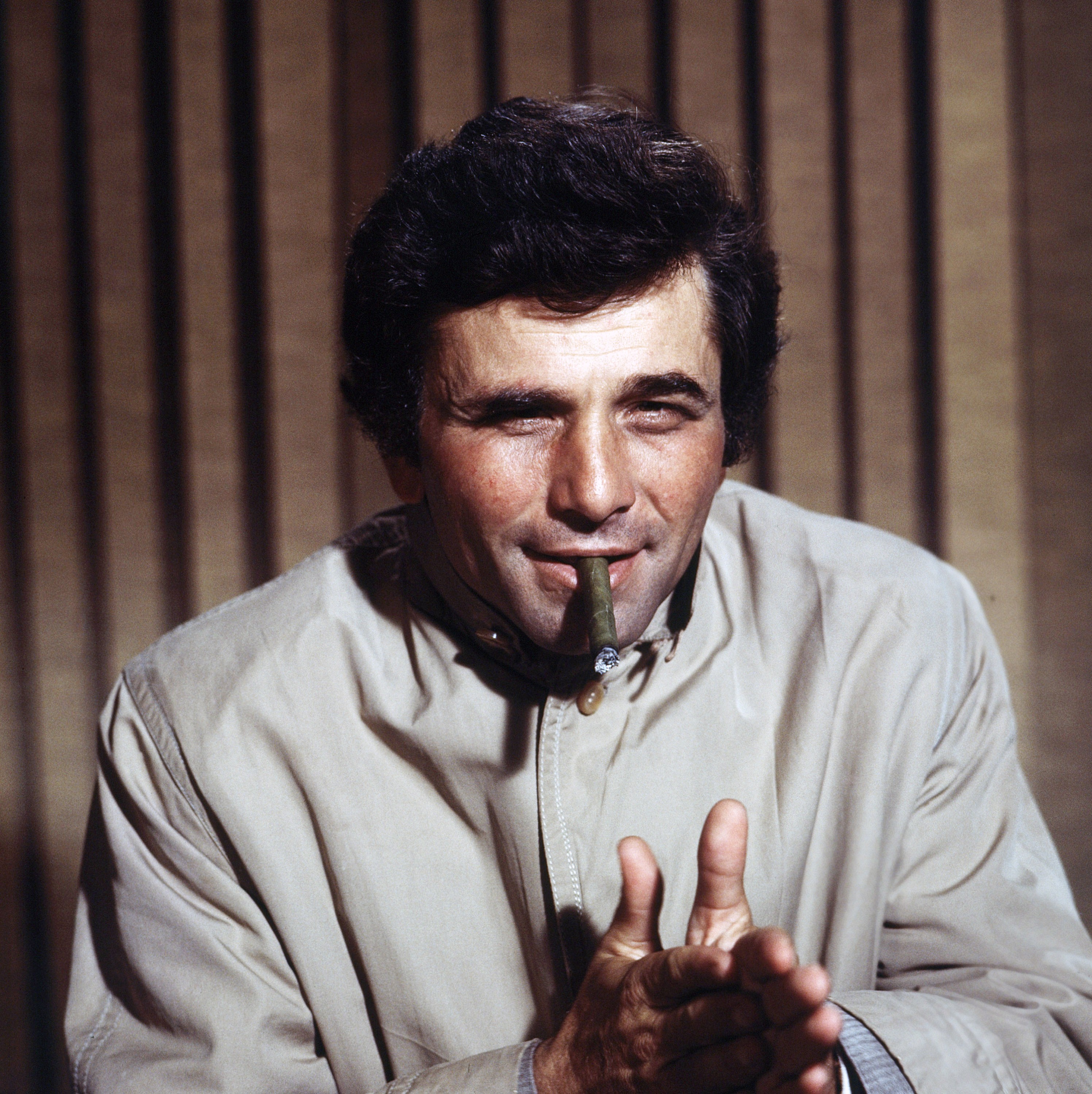Peter Falk smokes a cigar and puts his hands together as Columbo.